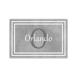 May include: Gray doormat with a white border and the letter "O" in the center. The text "Orlando" is written below the letter.