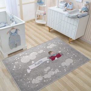 May include: A gray and white nursery rug with a cartoon airplane, clouds, and stars. The airplane has a red body and a white banner that says "Austin".