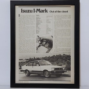 May include: A framed vintage magazine advertisement for the Isuzu I-Mark car. The black and white print features the headline Isuzu I-Mark Out of the closet, technical specifications, an interior view, and a side profile of the two-door vehicle.