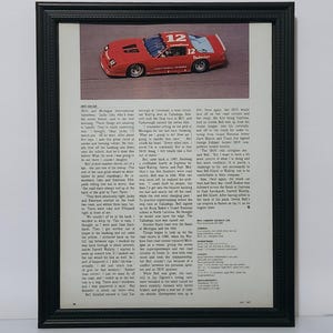 May include: A framed vintage magazine article featuring a red number 12 race car on a track. The page includes detailed text columns about IROC racing history, technical specifications for the Chevrolet Camaro, and a black decorative frame.