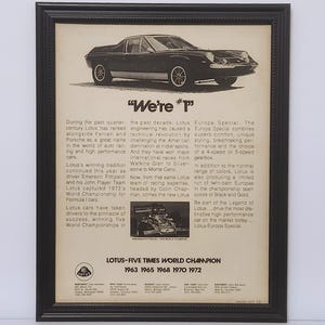 May include: Framed vintage advertisement for Lotus Europa Special. The black and white image features a sleek car and text highlighting the car's performance and racing success, including the text "We're #1". The frame is black.
