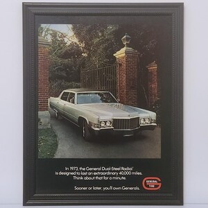 May include: Framed vintage advertisement featuring a silver car parked in front of a brick gate. The ad includes text about General Dual-Steel Radial tires, designed to last 40,000 miles. The General Tire logo is visible.