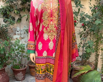 May include: A vibrant pink embroidered salwar kameez ensemble. The long-sleeved tunic features gold embroidery and a floral border. The outfit includes matching pants and a sheer dupatta in shades of orange and pink. The sleeves have green trim.