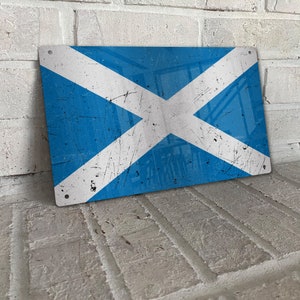May include: A blue and white distressed metal sign featuring the Scottish flag. The flag has a white cross on a blue background.