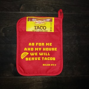 May include: Red pot holder with the text "As for me and my house we will serve tacos" and a small taco graphic. The text "Salsa 24:7" is at the bottom. A small Old El Paso taco seasoning packet is attached to the pot holder.