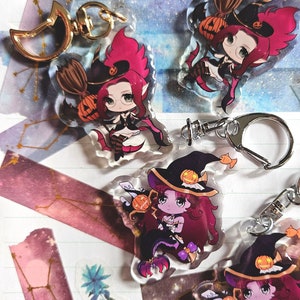 May include: Four Halloween-themed keychains featuring a witch with red hair and a black dress. Each keychain has a different pose and a pumpkin on their hat. The keychains are made of clear acrylic and have a gold metal ring.
