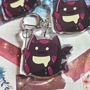 May include: Three purple and pink cartoon devil cat keychains with a small pitchfork and a silver key ring.