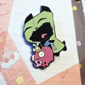 Puede incluir: Personaje de dibujos animados verde y negro con un cerdo rosa y un insecto amarillo en la espalda. El personaje sonríe y tiene la boca cosida. El cerdo tiene tres ojos y un hocico rosa.