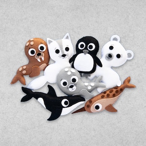 May include: A set of felt animal toys featuring a brown walrus, a white arctic fox, a black and white penguin, a white polar bear, a gray seal, and a brown narwhal.