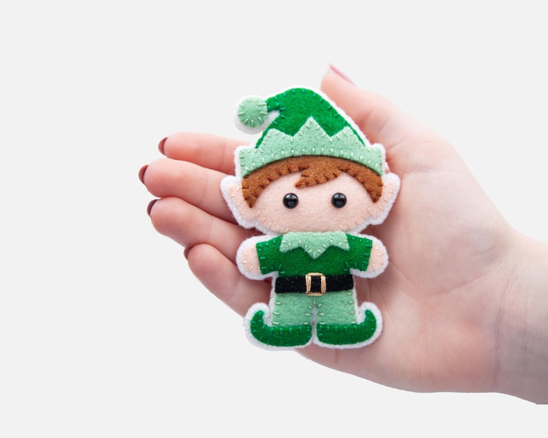 May include: A felt elf ornament with a green hat, brown hair, and a green and white outfit. The elf is holding a small red and white candy cane.