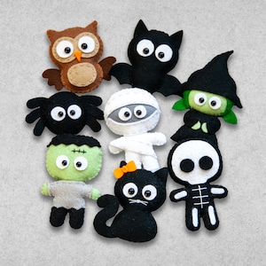May include: A set of nine felt Halloween characters, including a black bat, a green witch, a white mummy, a black spider, a green Frankenstein, a black cat, a brown owl, a white skeleton, and a black and white ghost.