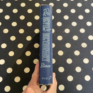 May include: A vintage hardcover book titled "The Devil's Dictionary" by Bierce. The book has a blue cover with white lettering. The word "World" is printed at the bottom of the book.