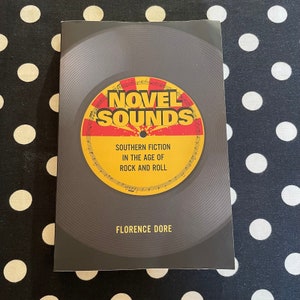 May include: A book titled "Novel Sounds: Southern Fiction in the Age of Rock and Roll" by Florence Dore. The cover features a stylized vinyl record with a red and yellow design.