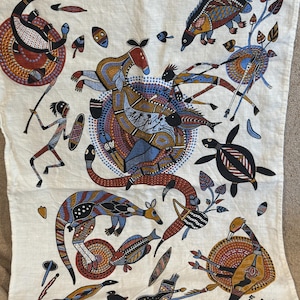May include: Cream-colored textile featuring an Aboriginal art design. The artwork depicts various animals and figures in a colorful, dot-painted style. The text "HUNTER DREAMING" is at the bottom, with "Churinga AUSTRALIA" below it.