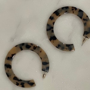 May include: A pair of large hoop earrings with a tortoiseshell pattern. The earrings are made of a brown and black plastic material.