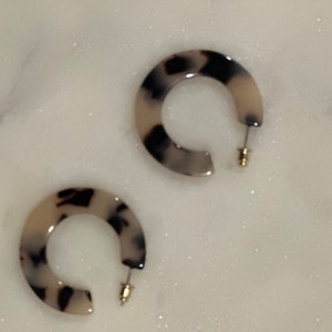 Può includere: Un paio di orecchini a cerchio in resina con motivo bianco e nero. Gli orecchini hanno un perno dorato.