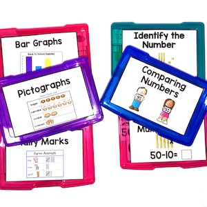 以下が含まれることがあります： 4つのカラフルなプラスチック製のトレイと透明な蓋があり、それぞれ異なる種類の数学アクティビティが含まれています。トレイには、「棒グラフ」、「絵グラフ」、「集計記号」、「数の比較」というラベルが付けられています。