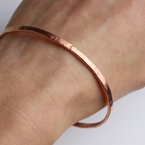 May include: A hammered copper bangle bracelet. The bracelet is a simple, minimalist design and is made from a single piece of copper.