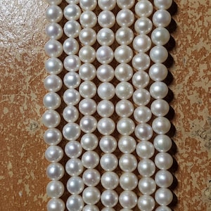 Peut inclure: Un brin de perles blanches, disposées en rangées, sur un fond brun.