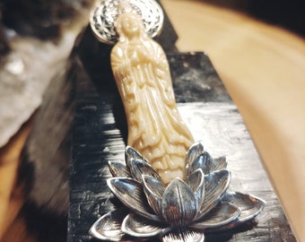 May include: A white carved pendant featuring a standing figure with a halo, set atop a silver lotus flower.