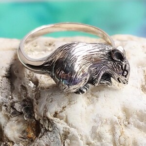May include: A silver ring featuring a detailed, three-dimensional mouse design. The mouse is depicted in a sitting position with its tail curled around its body.
