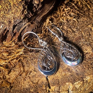 May include: A pair of silver teardrop earrings with a tree of life design and a crescent moon with a star. The earrings have a iridescent opal stone in the center.