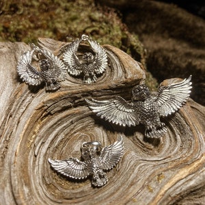 May include: Four silver owl charms with detailed wings and beaks. The charms are displayed on a piece of wood with a natural grain pattern.