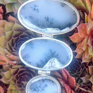 May include: A silver pendant necklace with three oval-shaped agate stones. The stones are a light blue color with dark gray dendritic patterns. The pendant is suspended from a silver chain.