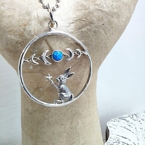May include: A silver necklace with a round pendant featuring a rabbit holding a star, a blue opal, and crescent moons.