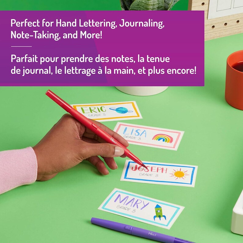May include: A hand holding a red pen over name tags with the names Eric, Lisa, Joseph, and Mary. The name tags have colorful borders and illustrations. The text at the top says, "Perfect for Hand Lettering, Journaling, Note-Taking, and More!"