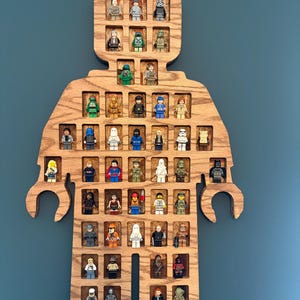 May include: A wooden display shelf shaped like a minifigure, featuring numerous rectangular cutouts designed to hold small plastic toy figures. The natural wood grain is visible throughout the structure, which contains a variety of colorful character figures arranged in rows within the individual compartments.