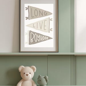 May include: Framed wall art with the words "LONG LIVE BOYHOOD" on three pennant flags in neutral tones. A white teddy bear and a green bear plush toy sit below the framed art on a green shelf.