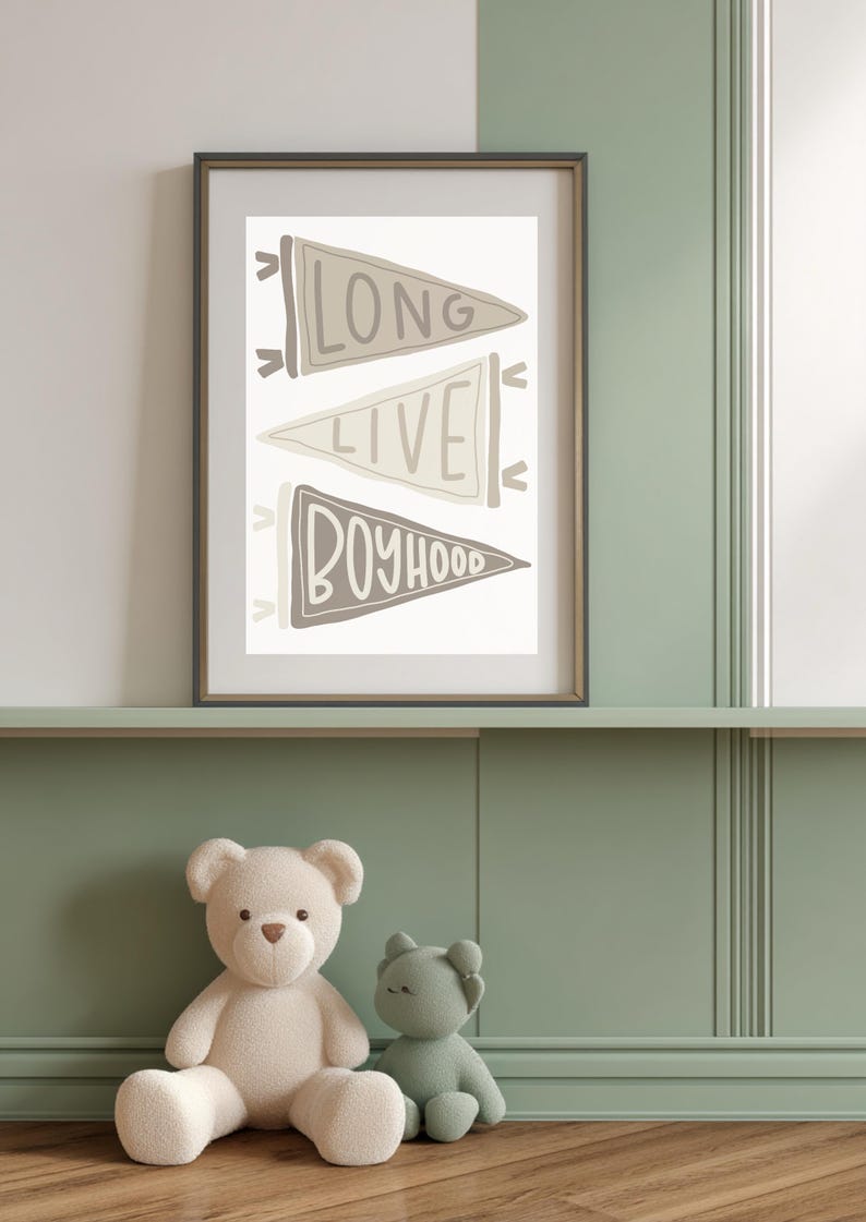 May include: Framed wall art with the words "LONG LIVE BOYHOOD" on three pennant flags in neutral tones. A white teddy bear and a green bear plush toy sit below the framed art on a green shelf.