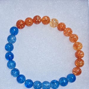 May include: A beaded bracelet featuring a gradient of colors. The bracelet transitions from blue to orange, with each bead displaying a speckled, glittery texture. The beads are strung together, forming a complete circle.