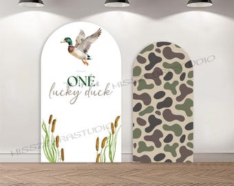 May include: Two large, arched decorative panels. One features a flying duck illustration with the text "One lucky duck." The other panel has a camouflage pattern in shades of green, brown, and tan. The panels are set against a white wall with hanging lights.