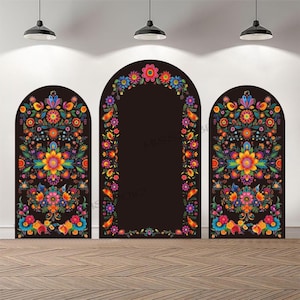 May include: Three black arch-shaped backdrops with vibrant floral designs. The colorful patterns include orange, yellow, blue, and pink flowers. The backdrops are set against a white wall and a wooden floor, illuminated by overhead lights.