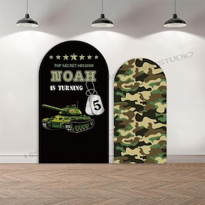 Pode incluir: Duas decorações de festa em arco. Um arco preto apresenta uma ilustração de um tanque verde, o texto "TOP SECRET MISSION", "NOAH IS TURNING" e etiquetas de identificação com o número 5. O outro arco tem um padrão de camuflagem.