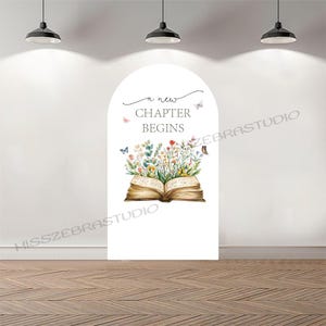 Puede incluir: Decoración mural blanca en forma de arco con una ilustración de un libro abierto con flores y mariposas de colores. El texto "a new CHAPTER BEGINS" está encima del libro. La decoración está colocada contra una pared blanca y un suelo de madera.