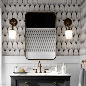 May include: A modern bathroom vanity with a black cabinet, gold hardware, and a marble countertop. A rectangular mirror with a gold frame hangs above the sink. The walls feature patterned wallpaper and sconces with white glass shades. A towel ring holds a gray towel.