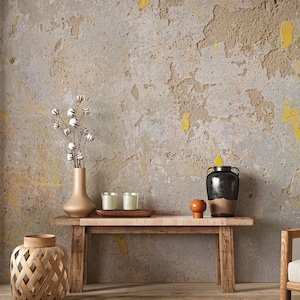 May include: A rustic wooden bench with a distressed beige wall in the background. The bench has a woven basket lantern, a vase with cotton stems, three candles, a small orange ceramic pot, and a black ceramic vase on top. A woven rug with fringe is on the floor in front of the bench.
