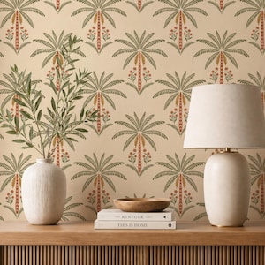 Op de afbeelding: Een beige muur met een herhalend patroon van groene en oranje palmbomen. Een witte vaas met groene takken staat op een houten plank, samen met boeken, een houten kom en een witte lamp.