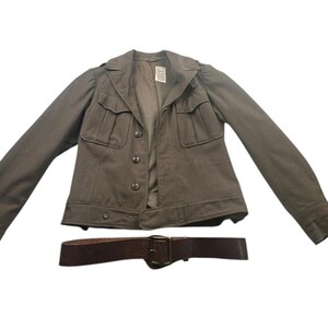 May include: A long-sleeved olive drab military-style jacket featuring a notched collar, two chest pockets with buttoned flaps, and a front button closure. Below the jacket is a dark brown leather belt with a metal buckle and a single prong.