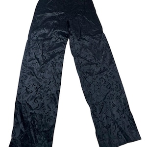 May include: Black wide-leg pants with a floral pattern. The pants are made of a shiny fabric and have a high waist. The floral design is a darker shade of black, creating a subtle contrast.
