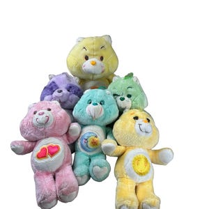 May include: A collection of plush Care Bears in various colors, including pink, yellow, green, and blue. Each bear has unique belly badges and expressions. The bears are soft and cuddly, perfect for collectors or children.