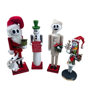 May include: Four decorative figures from The Nightmare Before Christmas: a Santa-clad Jack Skellington with Zero, a snowman Jack holding a Days Until Christmas calendar, a beige-clad Jack, and a Sally figure holding a small tree and basket.