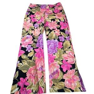 May include: Wide-leg pants with a vibrant floral pattern. The pants feature a black background with large pink, purple, and peach-colored flowers and green leaves. The pants have a button and zipper closure.