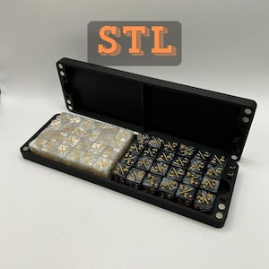 Op de afbeelding: Een zwarte, open dobbelsteendoos met twee compartimenten. Eén kant bevat doorzichtige dobbelstenen met gouden markeringen, de andere zwarte dobbelstenen met gouden markeringen. De tekst "STL" staat op de achtergrond.