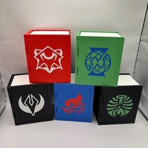 Op de afbeelding: Vijf kleurrijke, kubusvormige opbergdozen. Elke doos heeft een andere kleur: rood, groen, zwart, blauw en zwart. Elke doos heeft een witte bovenkant en een uniek wit of blauw grafisch ontwerp aan de voorkant.