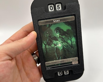 May include: Black and white counter with a black and white card holder. The card holder has a green and white card inside with the word "SPIRIT" and a green creature illustration. The counter displays the number "05".