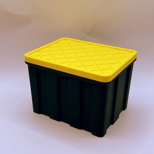 May include: A rectangular storage bin with a dark green base and a bright yellow lid. The lid features a raised diamond grid pattern, while the sides of the bin have vertical ribbed detailing. The container is constructed from rigid plastic.